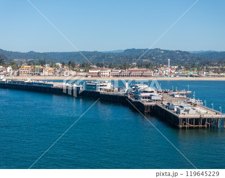 Aerial view of Santa Cruz Wharf extending into the Pacific Ocean, with buildings, boats, sandy beach, and vibrant town visible against distant hills. Aerial view of Santa Cruz Wharf extending into the Pacific Ocean, with buildings, boats, sandy beach, and vibrant town visible against distant hills. 119645229