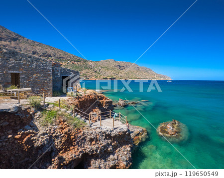エメラルドグリーンの海岸と崖の上に建つ石造りの家 (ギリシャ、クレタ島、プラカ) 119650549