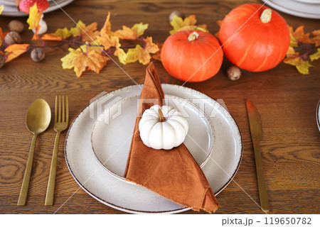 Autumn dinner setting with pumpkins, fall leaves, and elegant tableware for festive gatherings Autumn dinner setting with pumpkins, fall leaves, and elegant tableware for festive gatherings 119650782