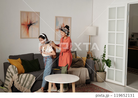 Mother Braiding Daughter's Hair in Cozy Living Room 119652131