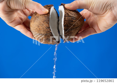 Hands open coconut, coconut water pour out, blue background 119652861
