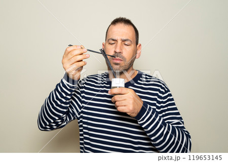 Bearded hispanic man in his 40s wearing a striped sweater smelling a set of scented aromatic diffuser reeds, isolated over beige background. Bearded hispanic man in his 40s wearing a striped sweater smelling a set of scented aromatic diffuser reeds, isolated over beige background. 119653145