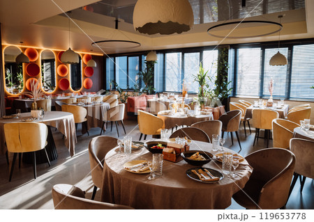Modern restaurant interior with elegant decor, tables, and lighting creating warm dining ambiance Modern restaurant interior with elegant decor, tables, and lighting creating warm dining ambiance 119653778