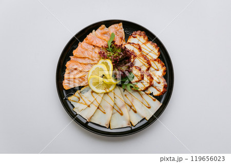 Gourmet seafood platter with salmon, white fish, and chicken slices garnished with lemon and greens 119656023