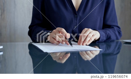 Businesswoman in dark blue blouse signing contract at the table. Close-up of a male executive signing a legal document on a glass desk. Business people concept 119656074