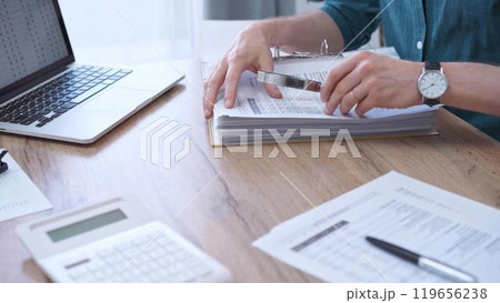 Businessman or auditor wearing green shirt is reviewing financial documents with magnifying glass. Business work process in bookkeeping office. Taxes 119656238