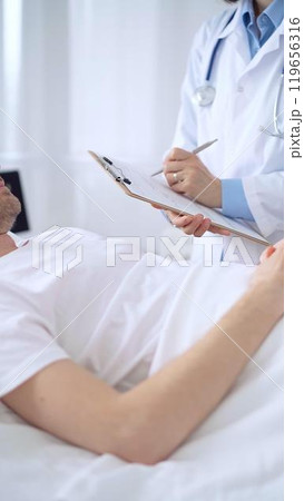 Female doctor writing medical report of patient lying in bed in hospital Female doctor writing medical report of patient lying in bed in hospital 119656316