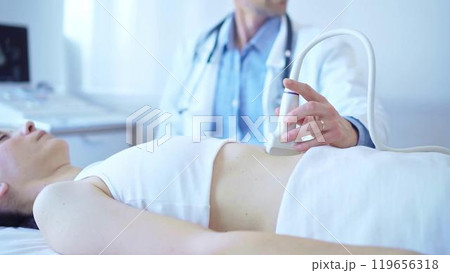 Doctor man wearing a white coat using an ultrasound machine on a female patient examining internal organs. Preventive therapy in medicine Doctor man wearing a white coat using an ultrasound machine on a female patient examining internal organs. Preventive therapy in medicine 119656318