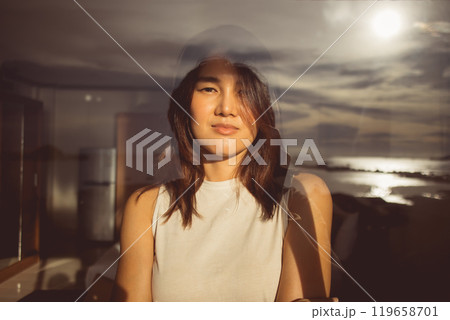 Woman looking out through the glass window which reflecting the sea view. 119658701