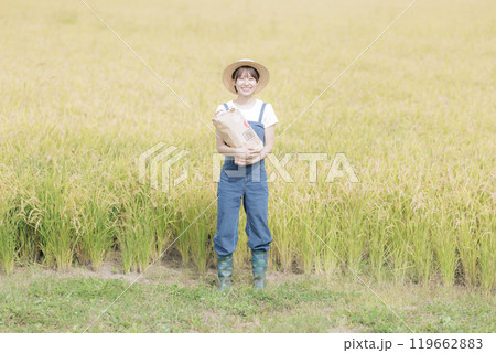 新米を持って田んぼの前に佇む若い女性 119662883