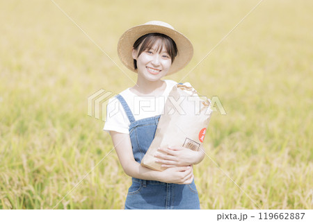 新米を持って田んぼの前に佇む若い女性 119662887