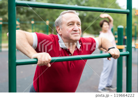 Elderly man doing leg stretching on the outdoor sports ground 119664222