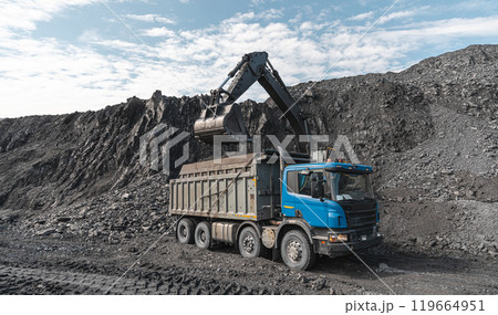 Large quarry dump truck and excavator. Big mining truck work coal deposit. Loading coal into body truck. Production useful minerals. Mining mining machinery to transport coal from open-pit production Large quarry dump truck and excavator. Big mining truck work coal deposit. Loading coal into body truck. Production useful minerals. Mining mining machinery to transport coal from open-pit production 119664951