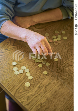 senior female sitting miserably at the table at home and counting coins. High quality photo 119666376