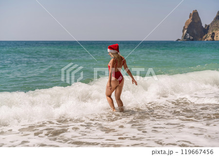 A woman in Santa hat on the seashore, dressed in a red swimsuit. New Year's celebration in a hot country A woman in Santa hat on the seashore, dressed in a red swimsuit. New Year's celebration in a hot country 119667456