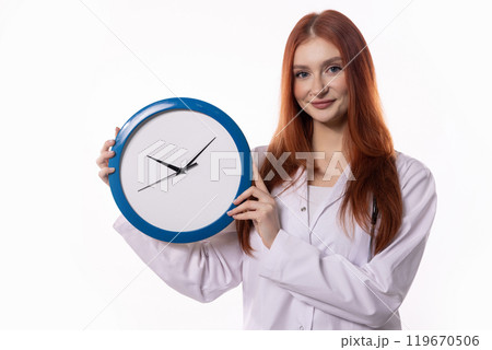 A Woman is Holding a Clock While Wearing a Lab Coat in an Official Professional Setting A Woman is Holding a Clock While Wearing a Lab Coat in an Official Professional Setting 119670506