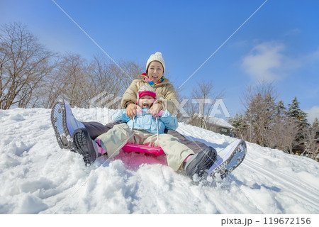 雪の公園でソリ遊びをする親子 119672156