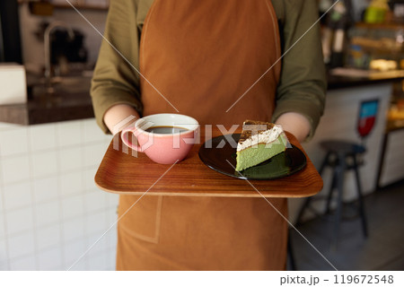 Cropped shot of woman barista giving wooden tray with coffee and cake portion Cropped shot of woman barista giving wooden tray with coffee and cake portion 119672548