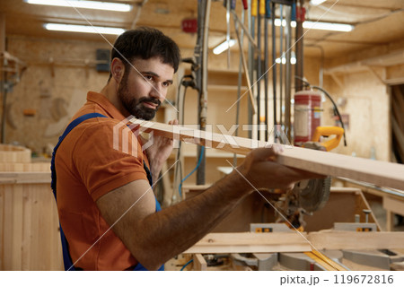 Portrait of artisan holding wooden timber plank over woodwork studio Portrait of artisan holding wooden timber plank over woodwork studio 119672816