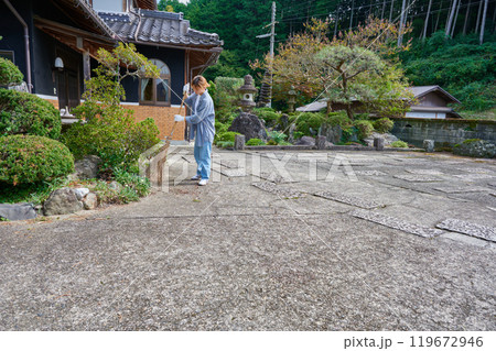 庭を掃き掃除する女性 田舎 古民家 旅館 暮らし 庭を掃き掃除する女性 田舎 古民家 旅館 暮らし 119672946
