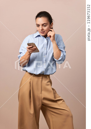 shocked pretty woman holding mobile phone looking at smartphone on beige background. shocked pretty woman holding mobile phone looking at smartphone on beige background. 119673152