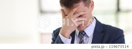 Depressive man in formal suit covers face with palm in office 119673514