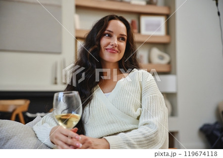 Woman enjoys a glass of white wine while relaxing at home in evening light 119674118
