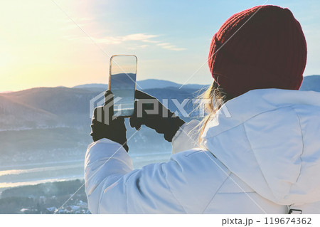 A person dressed in warm clothes is exploring winter landscapes and capturing them on a smartphone 119674362