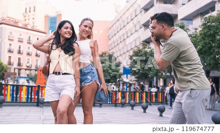 Man photographing stylish female friends on street in city 119674777