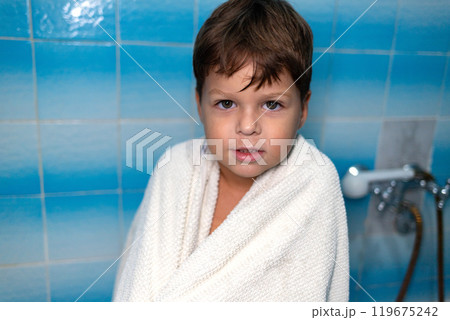 A 6-year-old boy stands in the bathroom wrapped in a terry towel. A 6-year-old boy stands in the bathroom wrapped in a terry towel. 119675242