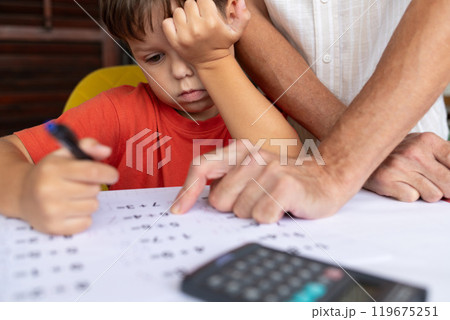 A father helps his 6-year-old son with his math homework. 119675251