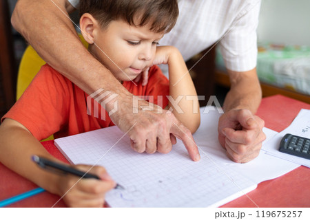 A junior schoolboy does his homework with the help of his father. 119675257