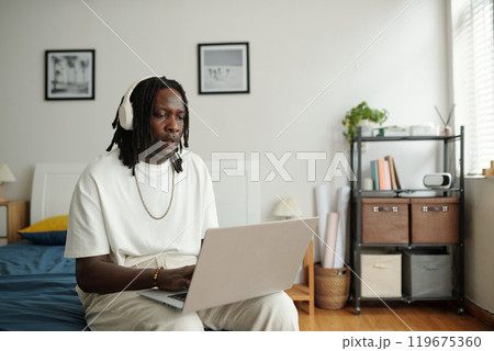Portrait of African American Man Using Laptop in Bedroom Portrait of African American Man Using Laptop in Bedroom 119675360