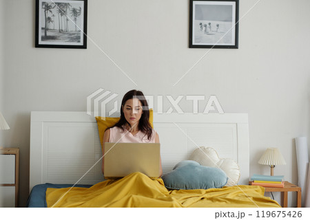 Young Woman Using Laptop in Cozy Bedroom Setting 119675426