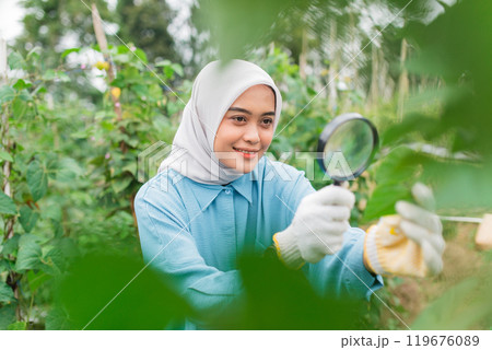 A Young Woman is Examining Plants with a Magnifying Glass in a Greenhouse 119676089