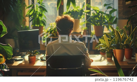 A person sits at a wooden desk surrounded by lush greenery, focusing on work while enjoying the natural light 119676742