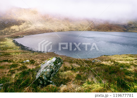 A serene lake lies nestled among rolling hills, enveloped in soft morning mist, creating a peaceful atmosphere in a remote countryside location. A serene lake lies nestled among rolling hills, enveloped in soft morning mist, creating a peaceful atmosphere in a remote countryside location. 119677781