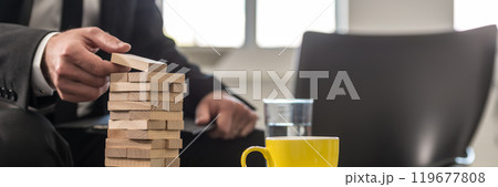 Wide panorama view of businessman in office building a tower of stacked blocks Wide panorama view of businessman in office building a tower of stacked blocks 119677808