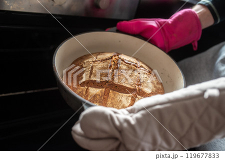 Closeup of a man taking a freshly baked home made bread out of the oven Closeup of a man taking a freshly baked home made bread out of the oven 119677833