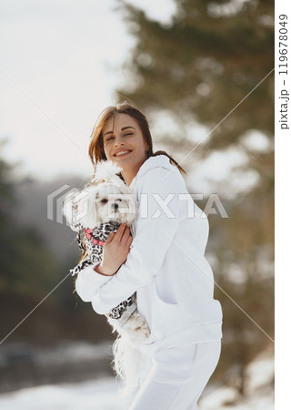 Cute girl walking in a winter park. Woman in a brown jacket. Lady with a dog. 119678049