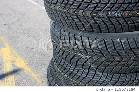 A set of four new winter tires are stacked on asphalt before the seasonal tire change. Same tread pattern tires detailed image 119678184