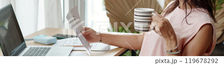 Examining Document While Holding Coffee Mug at Desk 119678292
