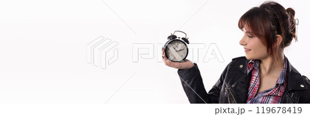 A Young Woman Enthusiastically Holding an Alarm Clock While Dressed in a Trendy Outfit 119678419