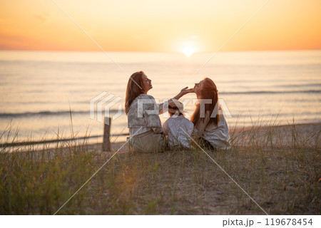 Back view of two caucasian female friends and a child enjoying sunset on the Baltic seashore.  119678454