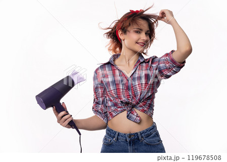 A young woman joyfully having fun while playfully using a hair dryer at home or in a salon 119678508