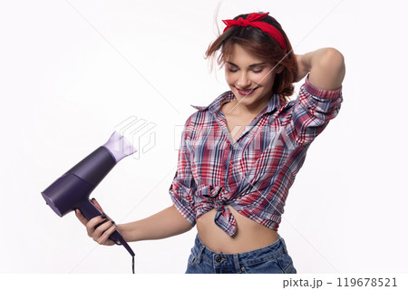 A Stylish and Young Woman is Drying Her Hair with a Hair Dryer in a Bright and Cheerful Setting 119678521