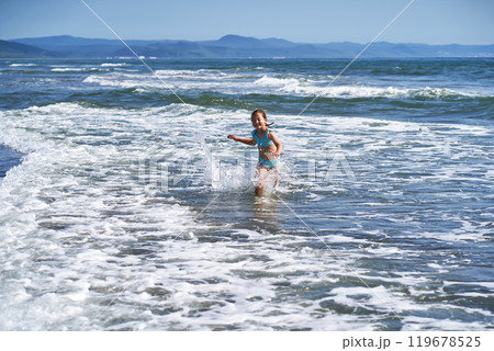An 8 year old girl in a swimsuit having fun in the sea waves. 119678525