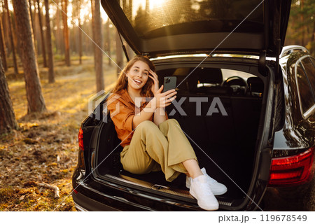 Beautiful woman in the trunk of a car enjoying nature in the forest. Adventure, technology concept. 119678549