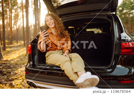 Beautiful woman in the trunk of a car enjoying nature in the forest. Adventure, technology concept. 119678564