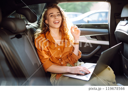 Beautiful business woman is using a laptop while sitting in the back seat of car. Freelance concept. Beautiful business woman is using a laptop while sitting in the back seat of car. Freelance concept. 119678566
